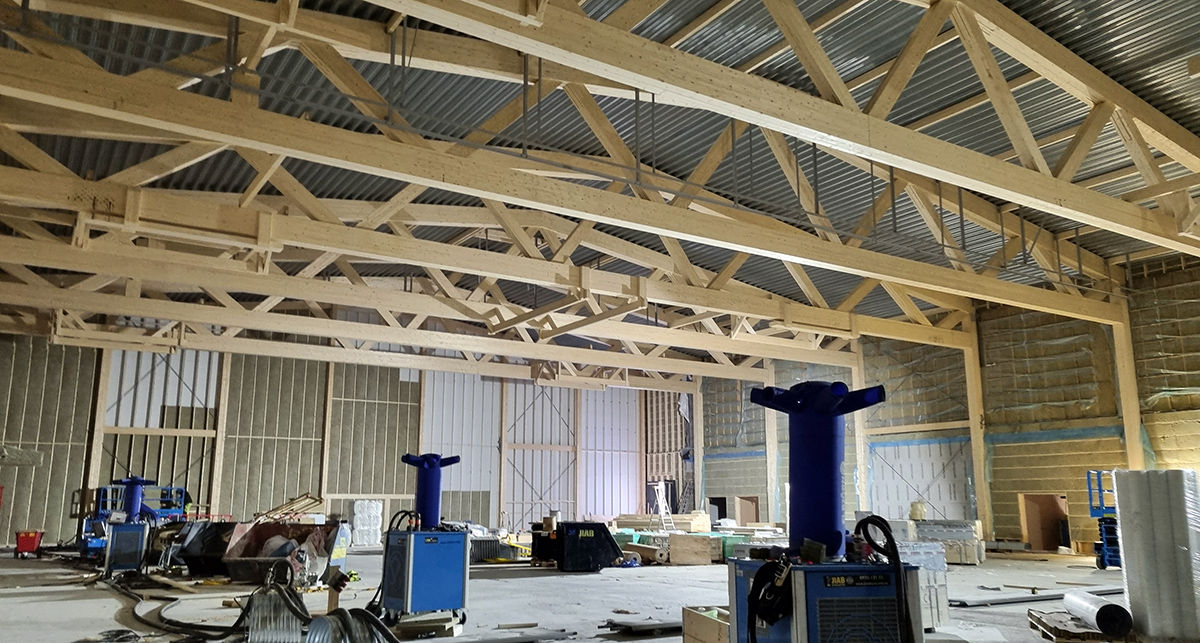 Inne i sporthallen som byggs för fullt. Kraftiga takstolar och byggmaterial på golvet